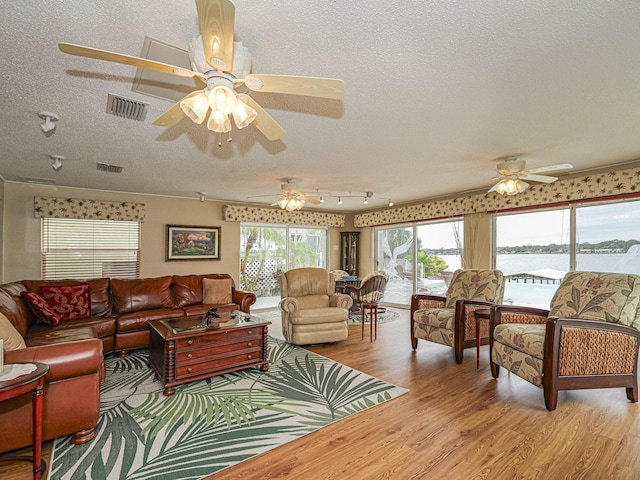 living area with a water view, a textured ceiling, visible vents, and wood finished floors