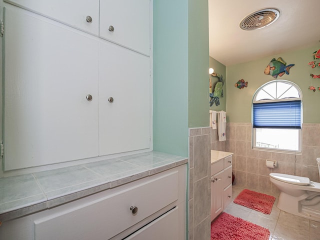 bathroom featuring tile patterned flooring, toilet, a wainscoted wall, visible vents, and tile walls