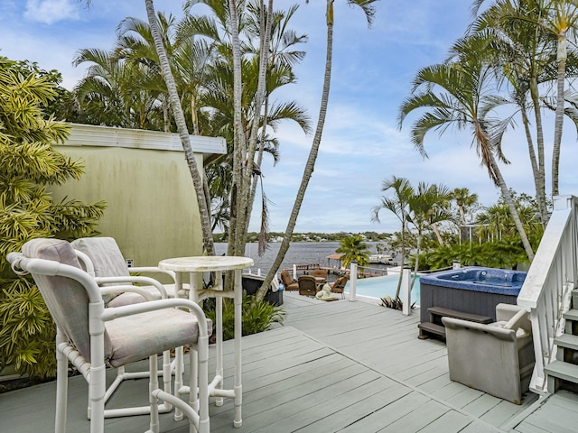 wooden terrace with a swimming pool with hot tub and a water view