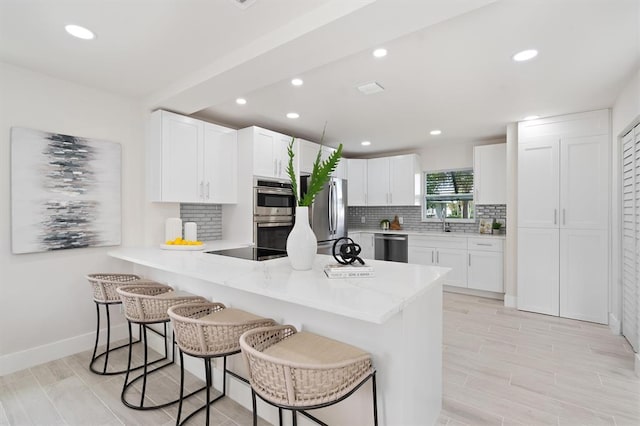 kitchen with kitchen peninsula, decorative backsplash, a breakfast bar area, stainless steel appliances, and white cabinets