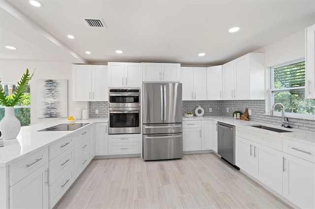 kitchen featuring backsplash, sink, white cabinetry, stainless steel appliances, and light stone counters