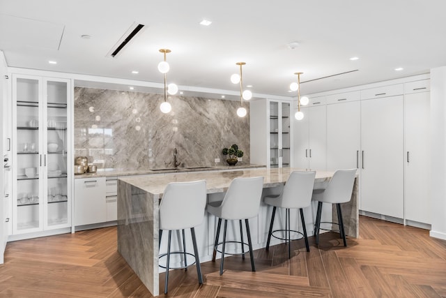 kitchen with a spacious island, decorative light fixtures, white cabinetry, sink, and light parquet floors