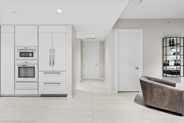 kitchen with paneled built in refrigerator, white cabinetry, light tile patterned floors, and multiple ovens