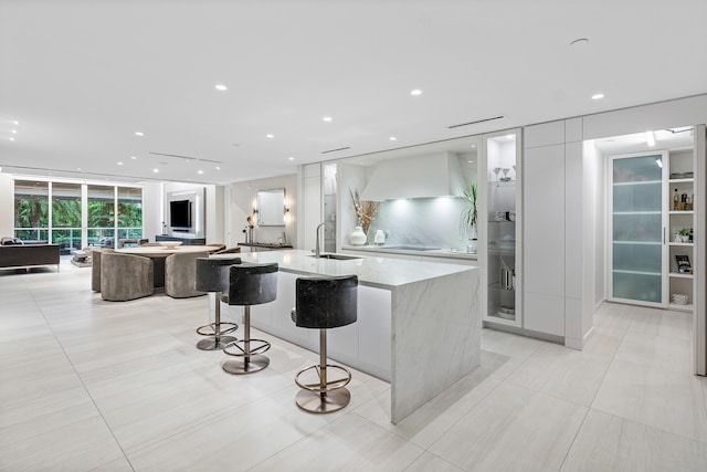 kitchen featuring light stone countertops, a large island with sink, a kitchen bar, white cabinetry, and floor to ceiling windows