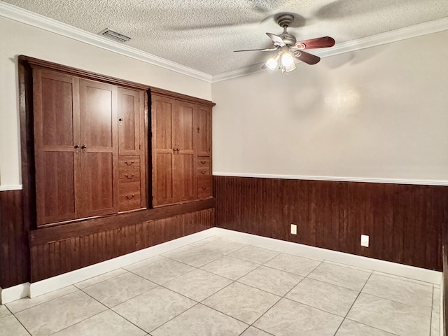 spare room with wood walls, a textured ceiling, light tile patterned floors, ornamental molding, and ceiling fan