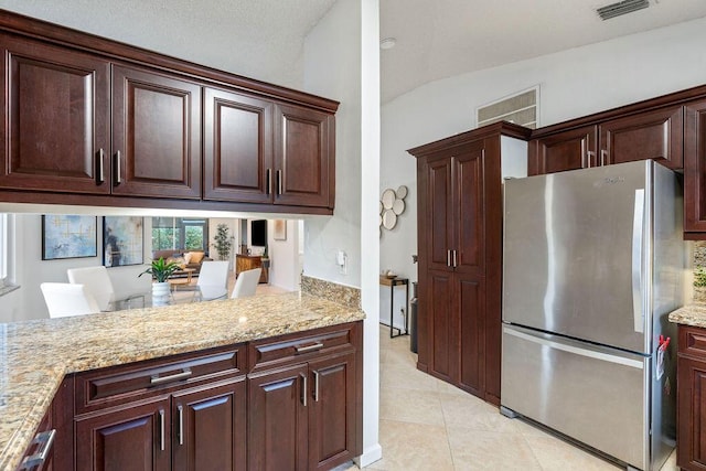 kitchen featuring light stone counters, stainless steel fridge, lofted ceiling, and light tile patterned flooring