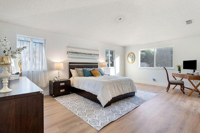 bedroom featuring light hardwood / wood-style floors, a textured ceiling, and multiple windows