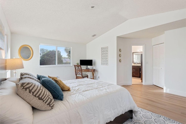 bedroom featuring light hardwood / wood-style floors, ensuite bath, a closet, and lofted ceiling