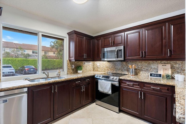 kitchen featuring light stone countertops, light tile patterned floors, decorative backsplash, sink, and stainless steel appliances