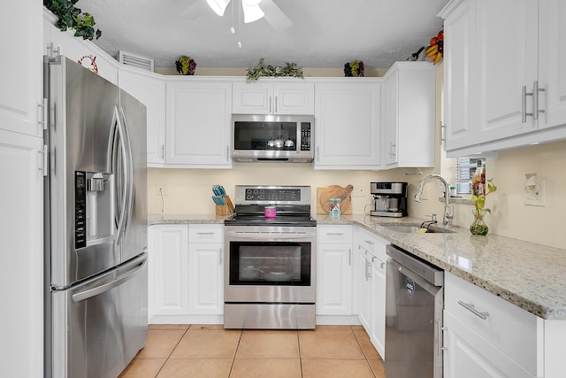 kitchen with sink, light tile patterned floors, light stone countertops, stainless steel appliances, and white cabinets