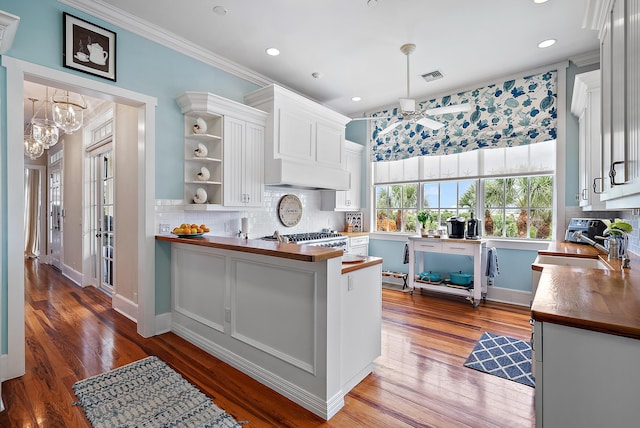 kitchen with kitchen peninsula, pendant lighting, white cabinets, dark wood-type flooring, and butcher block counters