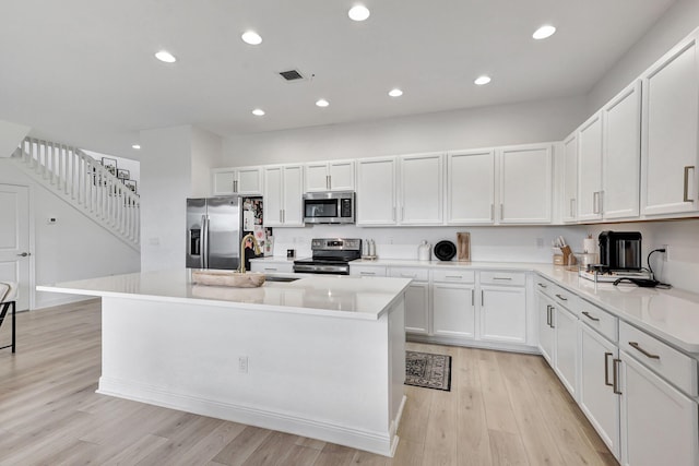 kitchen with white cabinets, appliances with stainless steel finishes, and an island with sink