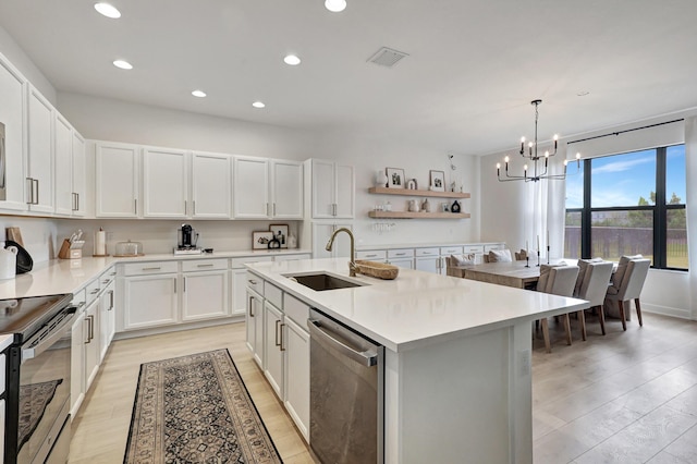 kitchen with white cabinetry, a center island with sink, stainless steel appliances, hanging light fixtures, and sink