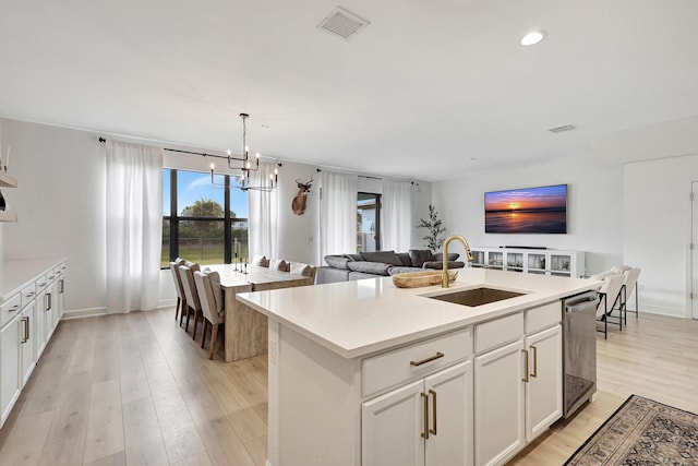 kitchen with a kitchen island with sink, dishwasher, hanging light fixtures, white cabinets, and sink