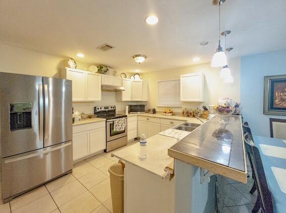 kitchen with white cabinets, stainless steel appliances, hanging light fixtures, kitchen peninsula, and light tile patterned floors