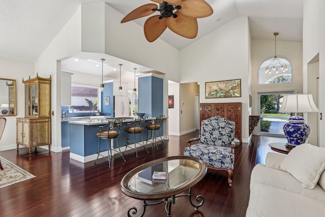 living room with ceiling fan with notable chandelier, dark wood-type flooring, and high vaulted ceiling