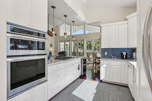 kitchen with lofted ceiling, pendant lighting, stainless steel appliances, white cabinets, and decorative backsplash