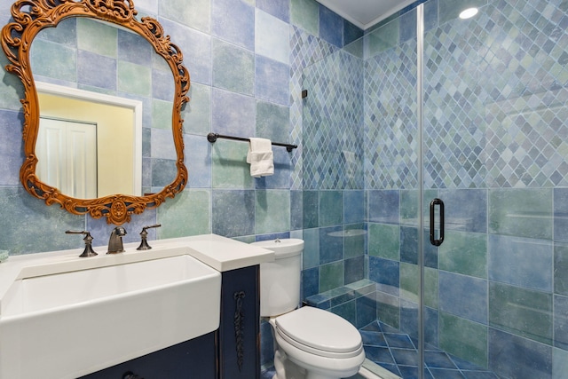 bathroom with a shower with door, vanity, tile walls, and toilet