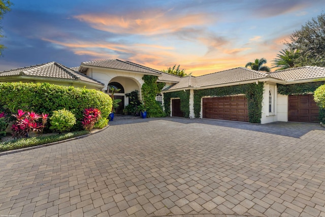 mediterranean / spanish home with decorative driveway, a tiled roof, and an attached garage