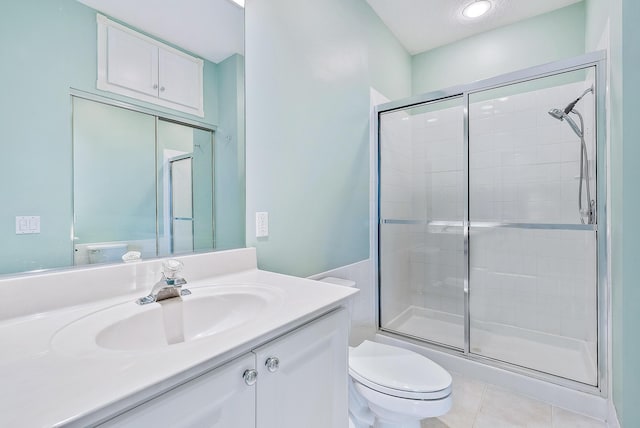 bathroom featuring tile patterned floors, vanity, toilet, and a shower with door