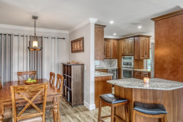 kitchen featuring wood-type flooring, pendant lighting, crown molding, double oven, and light stone counters