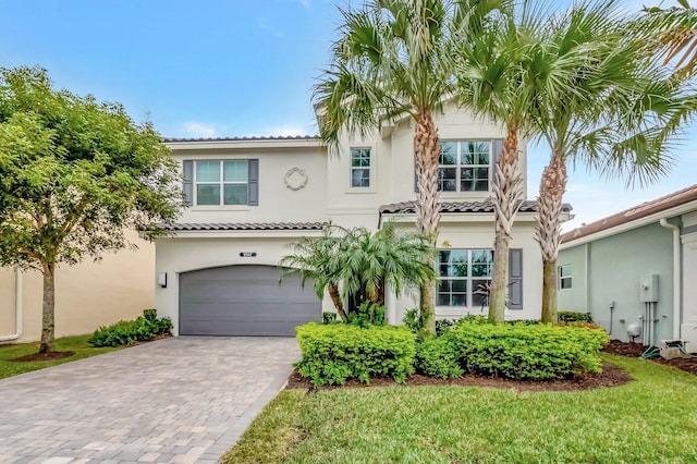 mediterranean / spanish-style house with a garage, decorative driveway, a tiled roof, and stucco siding