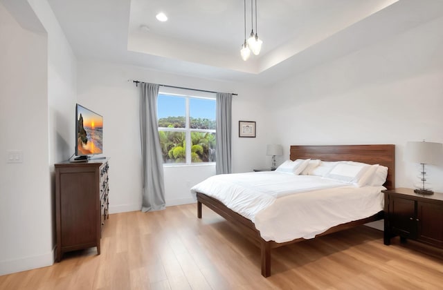 bedroom with light wood-type flooring, a raised ceiling, and baseboards