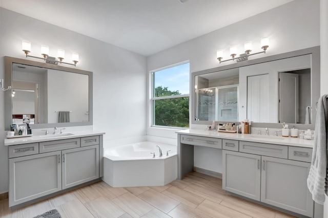 full bath featuring a bath, a shower stall, two vanities, and a sink