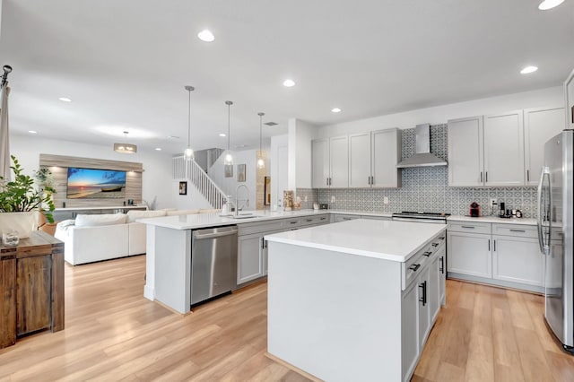 kitchen featuring kitchen peninsula, appliances with stainless steel finishes, decorative light fixtures, wall chimney exhaust hood, and a center island