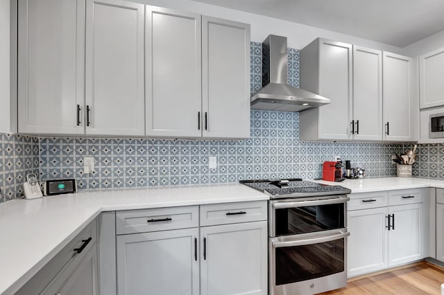 kitchen featuring double oven range, wall chimney exhaust hood, light hardwood / wood-style floors, and tasteful backsplash