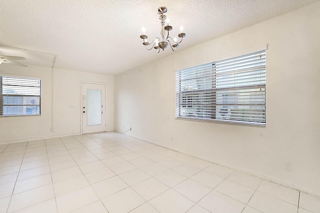 empty room featuring a textured ceiling, light tile patterned floors, and ceiling fan with notable chandelier