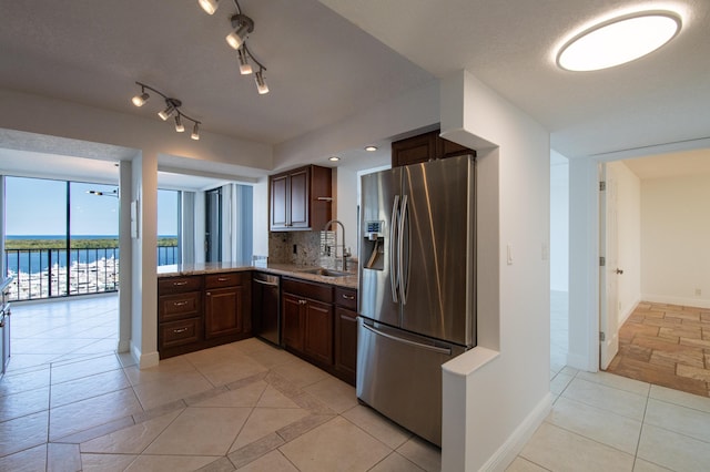 kitchen with baseboards, light stone countertops, decorative backsplash, stainless steel appliances, and a sink