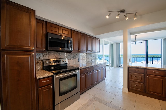 kitchen featuring a water view, light stone counters, appliances with stainless steel finishes, light tile patterned flooring, and decorative backsplash