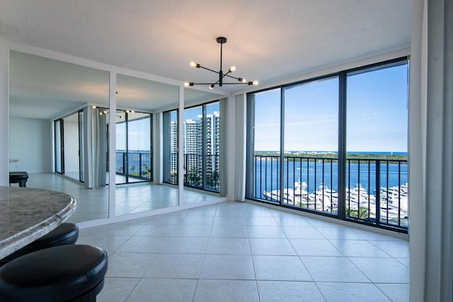 empty room featuring tile patterned flooring, a water view, an inviting chandelier, and expansive windows