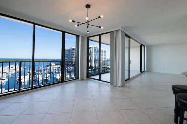 tiled empty room with expansive windows, a water view, a textured ceiling, and a chandelier