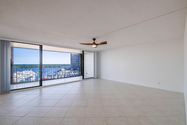 unfurnished room featuring light tile patterned floors, a ceiling fan, floor to ceiling windows, a water view, and a textured ceiling