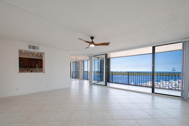 empty room with a water view, a wall of windows, ceiling fan with notable chandelier, and light tile patterned floors