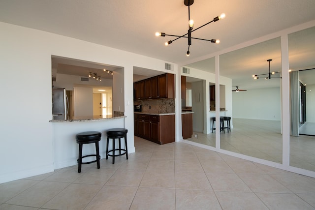 kitchen with light tile patterned floors, stainless steel fridge, light stone counters, tasteful backsplash, and kitchen peninsula