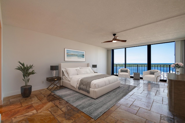 bedroom with a wall of windows, ceiling fan, access to exterior, a water view, and a textured ceiling