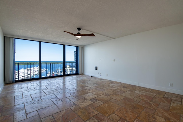 unfurnished room with floor to ceiling windows, a water view, ceiling fan, and a textured ceiling