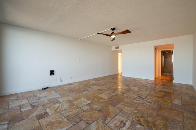 spare room featuring visible vents, baseboards, ceiling fan, stone tile floors, and a textured ceiling