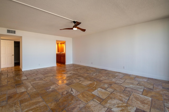 empty room featuring stone tile flooring, visible vents, baseboards, and ceiling fan