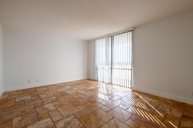 spare room featuring baseboards and stone tile flooring