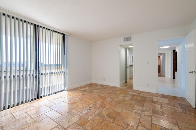 empty room with stone tile floors, visible vents, and baseboards