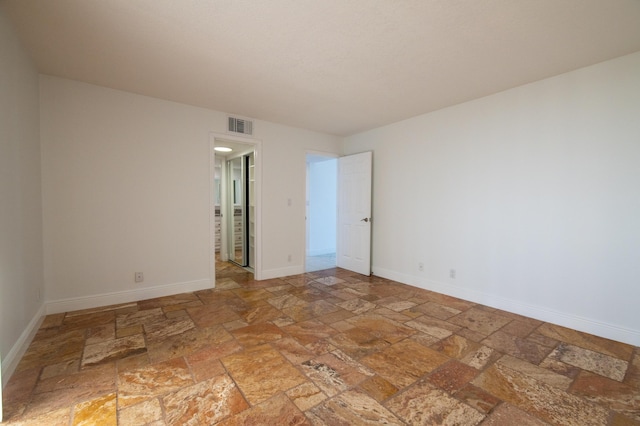 spare room with stone tile flooring, visible vents, and baseboards