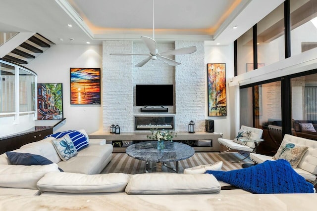 living room featuring a raised ceiling, a stone fireplace, and ceiling fan