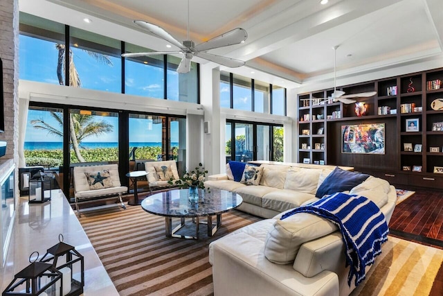 living room with built in features, ceiling fan, hardwood / wood-style floors, a high ceiling, and a water view