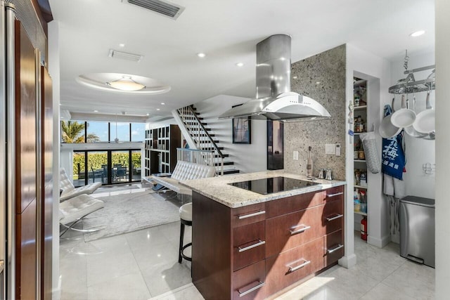 kitchen featuring a breakfast bar area, light stone counters, high end refrigerator, black electric cooktop, and island exhaust hood