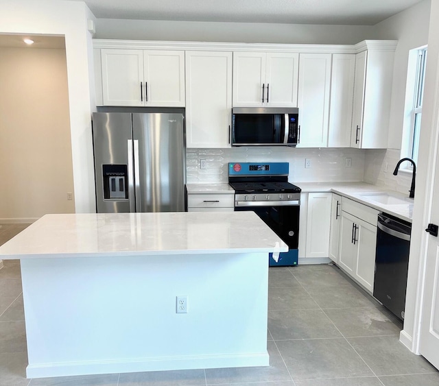 kitchen featuring a kitchen island, a sink, white cabinetry, appliances with stainless steel finishes, and decorative backsplash