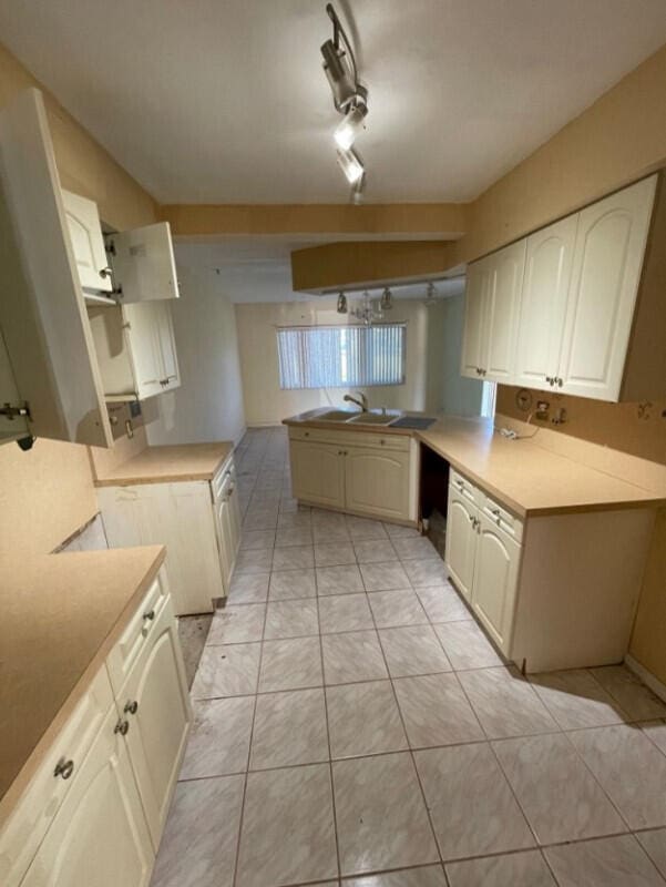 kitchen with light tile patterned flooring, rail lighting, kitchen peninsula, and sink